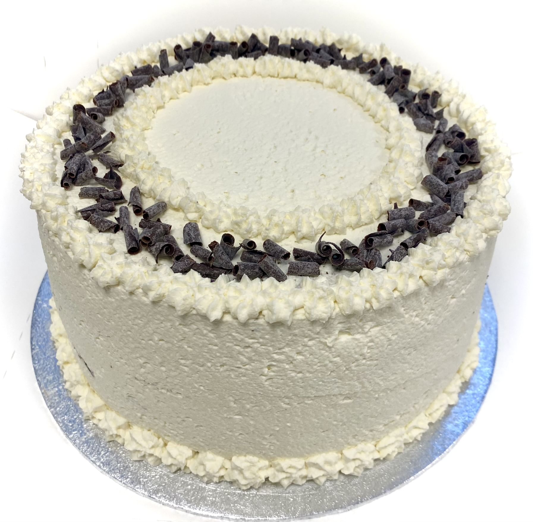 A round, plain white frosted cake with a simple design. The cake has small star-shaped frosting details along the top edge and the base. It is presented in a white box, with a silver cake board beneath it. The cake appears smooth and uniform in texture.
